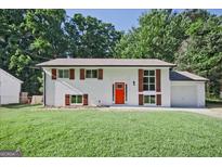Charming renovated home featuring a vibrant front door, white painted brick, green lawn, and lush, mature trees at 1349 Heather Cir, Riverdale, GA 30296