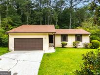 Charming one-story home with a brown roof, green lawn, and attached garage in a wooded setting at 9719 Dixon Industrial, Jonesboro, GA 30236