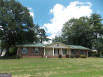 Charming single-story brick home featuring a green metal roof, blue shutters, and mature trees on a spacious lawn at 1253 Gatewood Drive Dr, Lawrenceville, GA 30043
