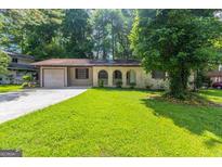 Charming single-story home with a lush green lawn, attached garage, and inviting arched entryway at 1105 Buckhurst Dr, Atlanta, GA 30349