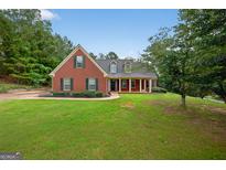 Charming brick home featuring a well-manicured lawn, mature trees, and classic architectural details under a bright blue sky at 65 Pecan Ln, Oxford, GA 30054