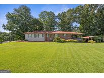 Ranch home with brick and vinyl siding, red metal roof, manicured lawn, and mature shade trees at 6674 Cowan Mill Rd, Winston, GA 30187