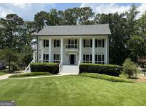 Stately two-story home featuring white siding, black shutters, a well-manicured lawn, and lush landscaping at 107 Edgewater Way, Peachtree City, GA 30269