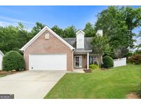 Charming brick home featuring an attached garage, well-manicured lawn, and mature trees at 320 Cloverwood Drive, Fayetteville, GA 30215