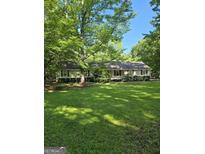 A well-manicured lawn and mature trees adorn this single-story home with red shutters and a quaint front porch at 140 Dixie Ln, Covington, GA 30014