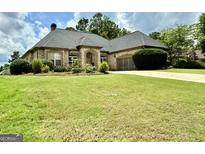 Beautiful brick home features a well-manicured lawn and a spacious driveway leading to an attached two-car garage at 6409 Caledon Ct, Locust Grove, GA 30248
