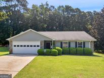 Charming ranch-style home with stone accents, lush green lawn, and manicured shrubbery creating inviting curb appeal at 2866 Rosecommons Dr, Hampton, GA 30228