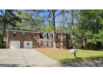 Brick home featuring an attached two-car garage and mature trees in a lush, green landscaped front yard at 2498 Robinhood Dr, Ellenwood, GA 30294