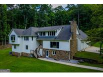 An exterior shot of a home with a stone chimney and front facade with lush green lawn and mature trees at 360 Darren Dr, Fayetteville, GA 30215