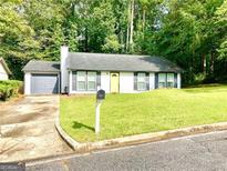 Charming ranch-style home featuring a well-manicured lawn, gray shutters, and a yellow front door at 3248 Brisbane Way, Lithonia, GA 30038