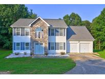 Charming two-story home featuring stone accents, blue shutters, a three-car garage, and a well-maintained front yard at 1067 Misty Meadows Pt, Hampton, GA 30228