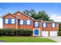 Traditional red brick home featuring a manicured lawn, blue shutters, and a two-car garage at 3796 Wolverton Cir, Lithonia, GA 30038