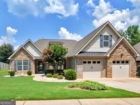 Charming brick and siding home featuring a manicured lawn, blossoming trees, and a two-car garage at 409 Brandy Ln, Mcdonough, GA 30253