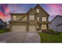 Beautiful two-story home featuring a three car garage and a stone and siding exterior with manicured lawn at 5915 Partners Pass, Cumming, GA 30028