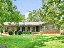 Charming brick home with arched entryways, green lawn and mature trees at 100 Homestead Pl, Rex, GA 30273