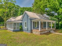 Charming blue home featuring a metal roof, inviting front porch, and a bright sunroom at 1128 Milstead Ne Ave, Conyers, GA 30012