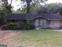 Modest single story house with a dark roof, an attached garage, and overgrown landscaping at 6553 Port A Prince Dr, Forest Park, GA 30297