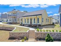 Charming yellow home featuring a welcoming front porch, brick stair accents, and beautifully landscaped front yard at 929 Hilltop Park Ct, Dacula, GA 30019
