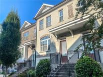 Charming brick townhome featuring a covered porch, black metal railings, and manicured greenery at 141 Laurel Crest Aly, Johns Creek, GA 30024