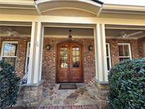 Inviting brick home entrance featuring a stone porch, double wooden doors, and ceiling fans at 3397 Holly Glen Dr, Dacula, GA 30019