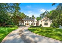 Elegant two-story white home featuring a circular driveway, manicured lawn and mature trees against a blue sky at 3488 Tuxedo Nw Rd, Atlanta, GA 30305