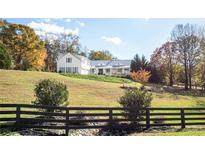 Charming white farmhouse with a metal roof on a sprawling green lawn, surrounded by colorful trees and a dark wooden fence at 1715 Sawnee Meadow Ln, Cumming, GA 30040
