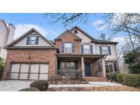 Charming two-story brick home featuring a covered front porch, attached garage, and mature landscaping at 2725 Monet Dr, Cumming, GA 30041