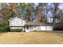 Gray house with white shutters, a two-car garage, and a front porch, nestled in a wooded area at 1472 Silver Maple Sw Ct, Lilburn, GA 30047