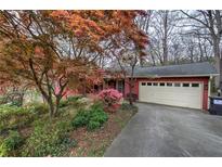 Charming red home featuring a two-car garage and well-manicured yard with vibrant flowering trees and bushes at 731 Willow Ridge Dr, Marietta, GA 30068