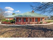 Brick ranch house with a green metal roof, large porch, and mature landscaping at 2620 Dr Bramblett Rd, Cumming, GA 30028