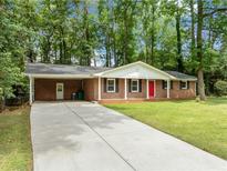 Brick ranch house with red door, driveway, and carport, nestled among lush green trees at 2683 Stardust Trl, Decatur, GA 30034