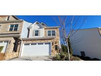 Two-story townhome with stone and light-colored siding, white garage door, and landscaping at 2343 Buford Town Dr, Buford, GA 30518