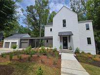 Modern white two-story home features a connected garage, a covered entrance, and fresh landscaping at 135 Cedarwood Ln, Roswell, GA 30075