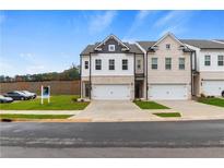 Two-story townhome with white and brick exterior, two-car garage, and landscaped lawn at 891 Eagle Ave, Riverdale, GA 30274