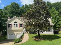Charming home with a two-car garage and front porch, surrounded by lush greenery and mature landscaping at 232 Taylors Farm Dr, Canton, GA 30115