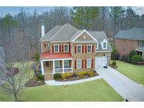 Charming two-story brick home with a red metal porch roof, a well-manicured lawn, and a basketball hoop on the driveway at 115 Hedgewood Ln, Canton, GA 30115