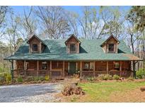 Rustic log cabin home with a green roof, large porch, and landscaped yard at 135 Fiddle Crk, Social Circle, GA 30025