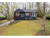 Charming, two-story home featuring a black exterior, brick chimney, and front yard with mature trees at 2597 Elsinore St, East Point, GA 30344