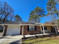 Charming single-story home featuring a brick facade, attached garage, and manicured front yard with mature trees under a blue sky at 432 Independence Dr, Jonesboro, GA 30238