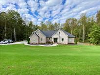 Brick house with large green lawn, driveway, and wooded area in background at 5710 Breitling Dr, Cumming, GA 30028