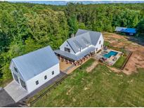 An aerial view of a modern farmhouse with a pool, metal roof, covered porch, and detached garage at 2731 Tribble Mill Rd, Lawrenceville, GA 30045