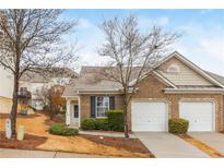 Charming brick townhome featuring a two-car garage and a well-manicured front yard with mature trees at 407 Red Coat Ln, Woodstock, GA 30188