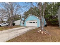 Light blue home with a two-car garage and a concrete driveway nestled in a wooded area at 2660 Burnstone Run, Lawrenceville, GA 30044