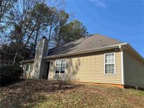 A single story home with beige vinyl siding and a brick chimney is nestled amongst mature trees at 20 Pebble Brooke, Covington, GA 30016