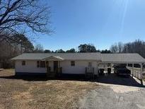 Ranch-style home with gray roof, carport, and mature trees, all under a bright blue sky at 1729 James Burgess Rd, Suwanee, GA 30024