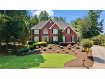 Charming two-story red brick home boasts manicured landscaping, lush greenery, and classic architectural details at 7215 Gresham Trce, Cumming, GA 30040