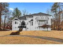 Elegant white home with a grand entrance, multiple balconies, and mature trees on a well-manicured lawn at 3670 River Mansion Dr, Peachtree Corners, GA 30096