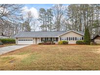 Ranch-style home featuring a large front yard, attached garage, and neutral siding, complemented by a white door and black shutters at 334 Nancy Sw Ct, Lilburn, GA 30047