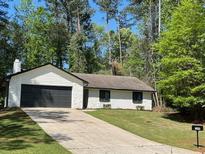 Charming single-story home featuring a dark garage door, well-manicured lawn, and beautiful surrounding trees at 1449 Albans Ct, Lithonia, GA 30058