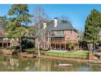 Brick home with a wooden deck overlooking a serene lake, complemented by lush landscaping and a private dock at 2143 Bogans Lake Path, Dunwoody, GA 30338